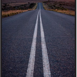 Könnte beinhalten: Eine lange, gerade Asphaltstraße mit weißen Doppelstrichen in der Mitte, die zu einem fernen Horizont mit einem farbenfrohen Sonnenuntergang führt.
