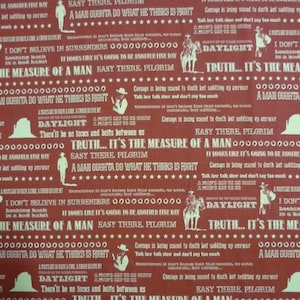May include: Red fabric with a repeating pattern of white text. The text includes the phrases "Daylight", "Truth... It's the measure of a man", "Easy there, pilgrim", and "A man oughta do what he thinks is right". A ruler with inches marked is visible at the bottom of the fabric.