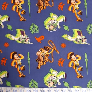 May include: Blue fabric with a repeating pattern of Toy Story characters, including Woody riding Bullseye, Buzz Lightyear in his spaceship, and Woody standing with his lasso. The fabric is measured with a tape measure.