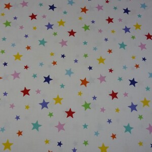 Könnte beinhalten: Weißer Stoff mit einem sich wiederholenden Muster aus bunten Sternen. Die Sterne sind in verschiedenen Farben, darunter Rot, Blau, Gelb, Grün, Pink und Türkis. Ein Lineal ist am unteren Rand des Bildes sichtbar.