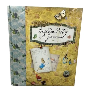 May include: A decorative journal with a floral patterned spine and a yellow cover featuring the text "Beatrix Potter A Journal". The cover includes a butterfly, illustrations of rabbits, and other decorative elements.