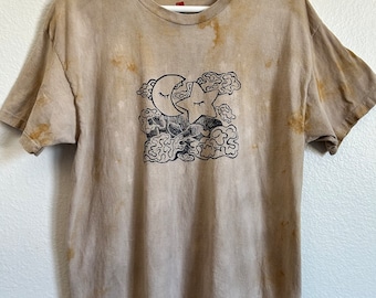 May include: A light brown t-shirt with a tie-dye pattern. The shirt features a black and white print of a crescent moon with a closed eye, a star, and clouds.