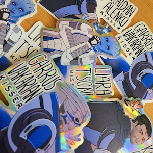May include: A collection of holographic stickers featuring characters from a science fiction video game. The stickers display various characters in action poses, with text including character names and the word "KISSER". The stickers have a shiny, iridescent finish.