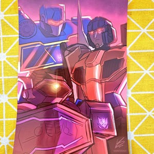 以下が含まれることがあります： 3体のトランスフォーマーロボットのデジタルイラスト。中央のロボットは赤とオレンジで、青い胸板をしています。左側のロボットは青で、黄色の胸板をしています。右側のロボットは紫で、青い胸板をしています。ロボットたちはピンクと紫の背景の前に立っています。