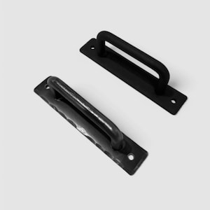 May include: Two black metal door pulls with a rectangular base and a rounded handle. The pulls are shown against a white background. Each pull has two holes for mounting.