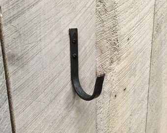 May include: A black metal hook is attached to a white wooden wall. The hook is shaped like a 'J' and has a rounded end.