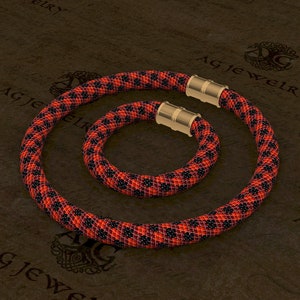 May include: A set of two beaded necklaces in a black and orange geometric pattern. The necklaces are made with small beads and have gold-toned clasps.