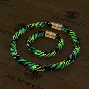 May include: A black and green beaded necklace and bracelet set with a geometric pattern. The necklace and bracelet have magnetic clasps.