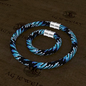 May include: A set of two beaded necklaces in a black and blue geometric pattern with silver magnetic clasps. The necklace is larger than the bracelet.