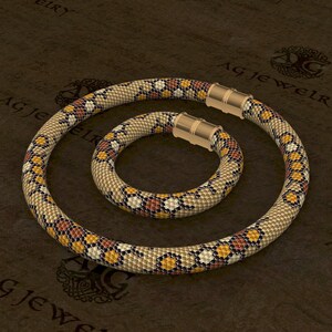 May include: A set of two beaded bracelets with a geometric pattern in shades of brown, yellow, and white. The bracelets have gold-toned magnetic clasps.