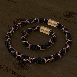 May include: A black and pink beaded necklace and bracelet set with gold magnetic clasps. The beads are arranged in a geometric pattern.