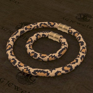 May include: A set of two beaded necklaces with a leopard print pattern. The necklaces are made of small, black, brown, and beige beads. The necklaces have gold-toned magnetic clasps.