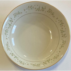 May include: Cream-colored ceramic bowl with a gold rim and delicate floral pattern. The design features small white flowers and green leaves arranged in a repeating pattern around the rim. A thin gold line borders the floral design.