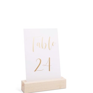 May include: A white card with gold lettering that reads "Table 24" is displayed on a wooden stand.