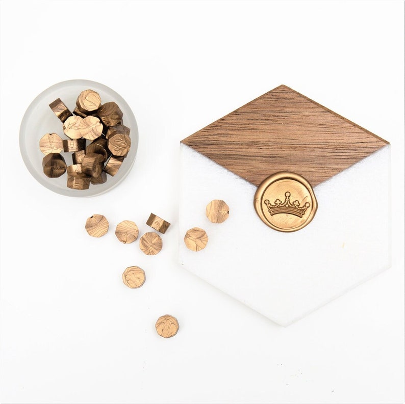 May include: A bowl of gold wax seals with a crown wax seal on a wooden and white surface.