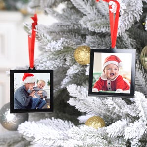 May include: Two black framed Christmas ornaments with photos of children wearing Santa hats. The ornament on the left shows a father and son, while the ornament on the right shows a baby boy.