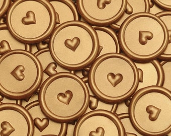 May include: A close-up of a pile of gold wax seals with a heart design. The seals are arranged in a random pattern and are all the same size.