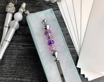 May include: A silver letter opener with a purple and pink beaded handle in a light blue gift box.