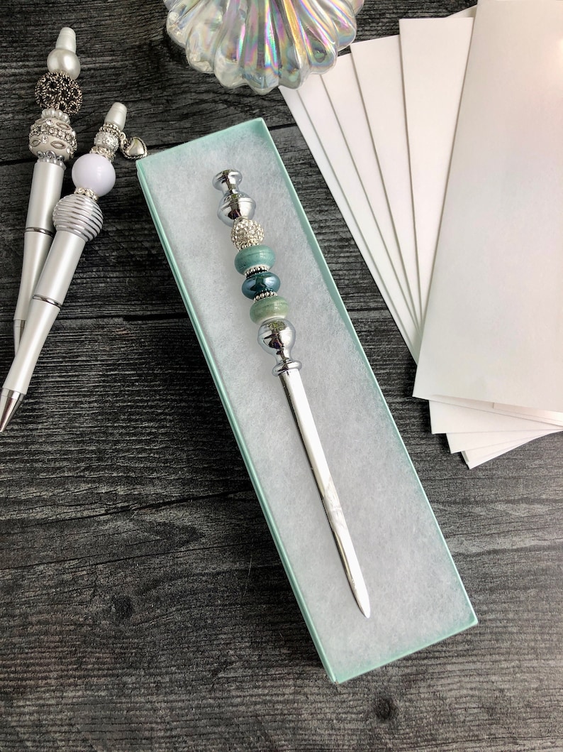May include: A silver letter opener with a decorative handle featuring turquoise and silver beads. The letter opener is in a light blue box.