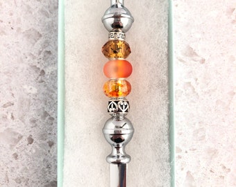 May include: A silver letter opener with a decorative top and orange and amber glass beads.