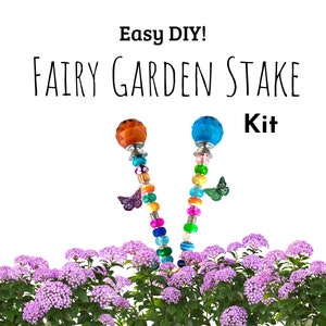 May include: Easy DIY! Fairy Garden Stake Kit featuring two colourful stakes, each topped with a crystal ball and decorated with beads and a butterfly charm. The stakes are shown against a background of pink flowers.