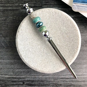 May include: A silver letter opener with a decorative handle featuring green and blue beads. The handle is adorned with rhinestones.