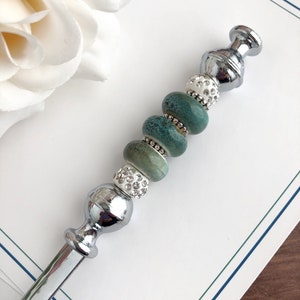 May include: A silver letter opener with a decorative handle. The handle is adorned with turquoise and white beads, some of which are embellished with rhinestones.