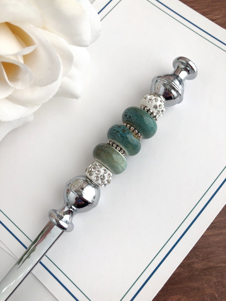 May include: A silver letter opener with a decorative handle. The handle is adorned with turquoise and white beads, some of which are embellished with rhinestones.