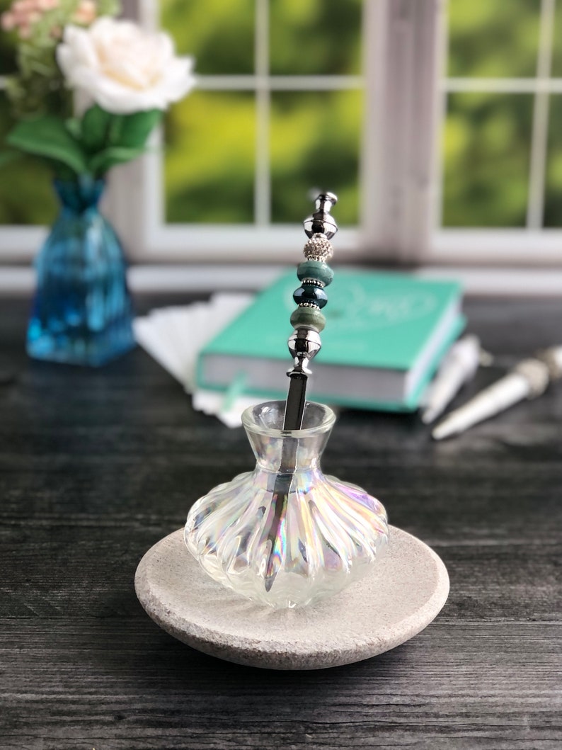 May include: A silver and green beaded pen holder in a clear iridescent glass bottle with a gray stone base.