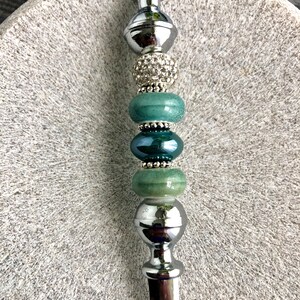 May include: A silver letter opener with a decorative handle. The handle is adorned with green and silver beads, including a bead with rhinestones.