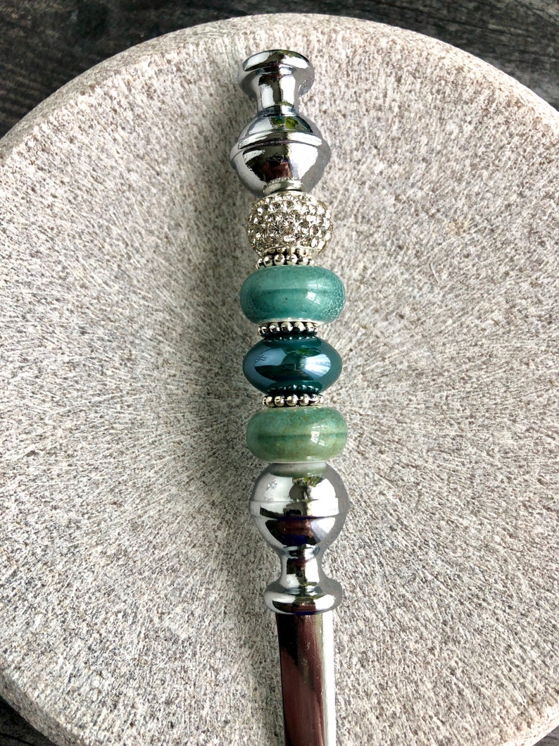 May include: A silver letter opener with a decorative handle. The handle is adorned with green and silver beads, including a bead with rhinestones.