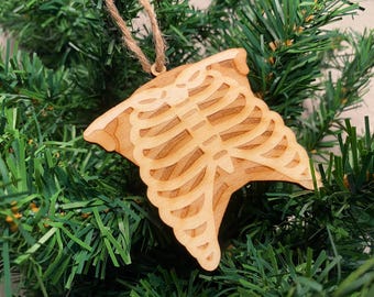 May include: A wooden Christmas ornament shaped like a ribcage. The ornament is light brown and has a rustic, hand-crafted look.