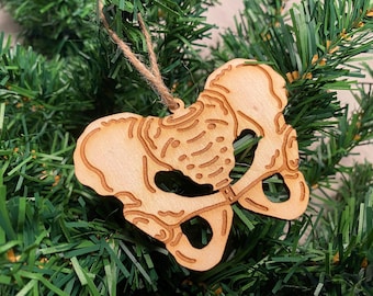 May include: A wooden Christmas bauble shaped like a human pelvis. The bauble is light brown and has a string attached for hanging.