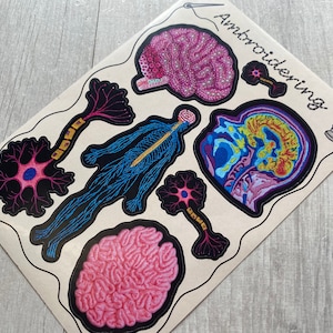 Puede incluir: Un conjunto de parches bordados de colores para planchar que presentan ilustraciones anat&oacute;micas del cerebro, una neurona y el sistema nervioso humano. Los parches est&aacute;n etiquetados como "Embroidering".