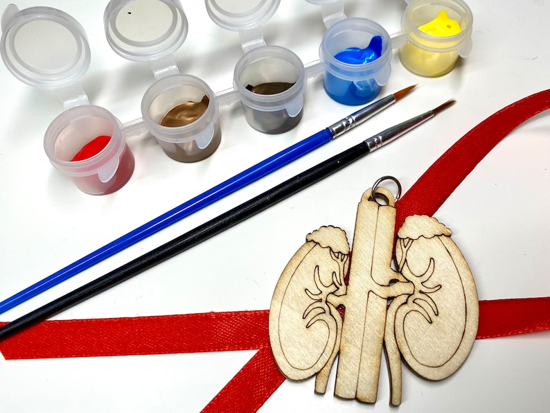 May include: A paint-your-own kit with small paint pots in various colors, two paint brushes, and a wooden kidney-shaped ornament with a red ribbon. The paint colors include red, brown, blue, and yellow.