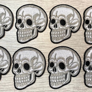 May include: Eight white embroidered skull patches with black eyes. The skulls are detailed with stitching and have a 3D effect.