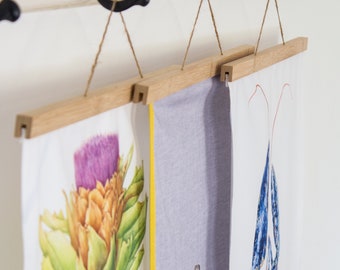 May include: Three wooden hanging picture frames with fabric prints. The left frame has a white background with a watercolor illustration of an artichoke. The middle frame has a light gray background. The right frame has a white background with a blue and red watercolor illustration of a lobster.
