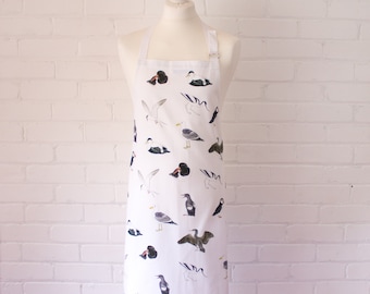 May include: White apron with a pattern of various seabirds, including gulls, puffins, and ducks. The apron has adjustable straps and a pocket.