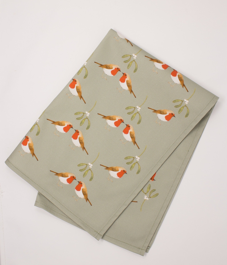 May include: A green tea towel with a repeating pattern of red robins kissing under sprigs of mistletoe.