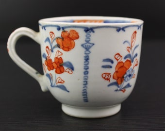 May include: A white porcelain teacup with a blue and orange floral design. The cup has a rounded shape and a handle.