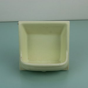 May include: A white ceramic soap dish with a rounded rectangular shape. The dish has a slight lip around the edge.