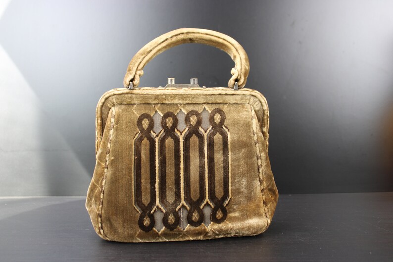 May include: A vintage brown velvet handbag with a geometric design. The handbag has a top handle and a clasp closure.