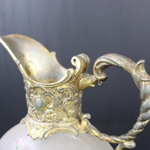 May include: A silver and gold pitcher with an ornate design and a twisted handle.