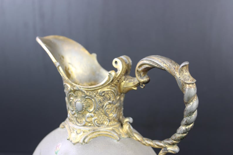 May include: A silver and gold pitcher with an ornate design and a twisted handle.