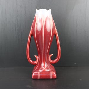 Peut inclure: Un vase en céramique rouge et blanc avec deux anses. Le vase a un design unique et stylisé et une finition brillante.