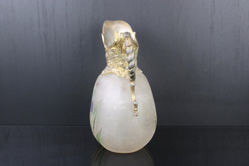 May include: A frosted glass jug with a gold and silver handle. The jug has a floral design painted on the side.