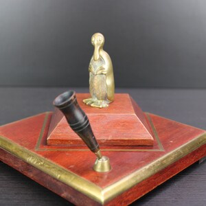 Op de afbeelding: Een houten bureauset met een messing pinguïnbeeldje en een zwarte penhouder.