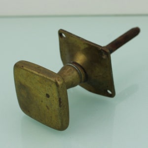 Peut inclure: Une poignée de porte en laiton avec une poignée carrée et une plaque de base carrée. La poignée est fixée à une tige métallique.