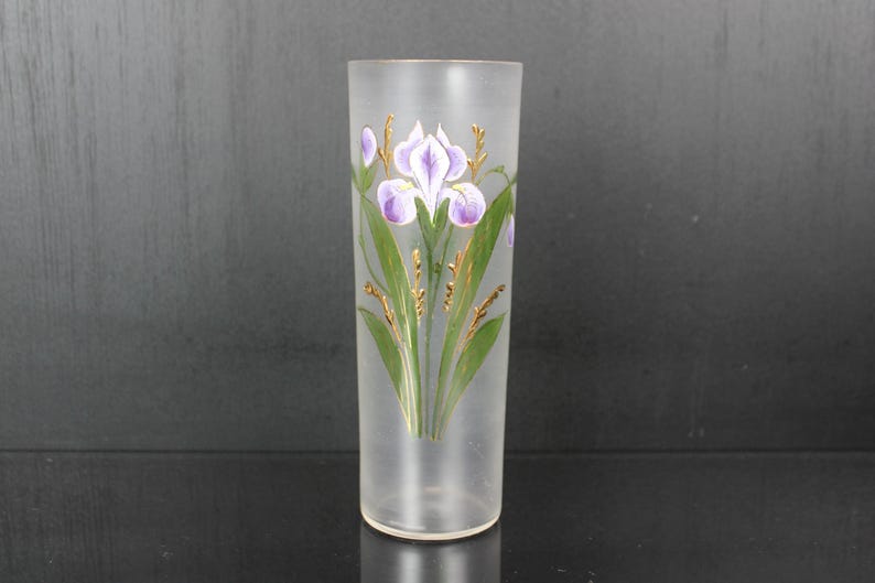 Pu&ograve; includere: Un vaso di vetro smerigliato con un motivo floreale dipinto a mano. Il design presenta fiori di iris viola con foglie verdi e dettagli dorati. Il vaso &egrave; cilindrico e misura circa 20 cm di altezza.