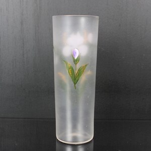 Pu&ograve; includere: Un vaso di vetro smerigliato con un motivo floreale dipinto. Il motivo presenta un fiore viola con foglie verdi e dettagli dorati. Il vaso &egrave; cilindrico e ha una finitura liscia e smerigliata.